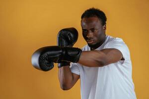 Practicing the boxing, punch. Black guy is against yellow background photo