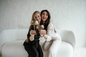 In black,and white clothes, with drink, celebrating. Two happy young female best friends are indoors photo