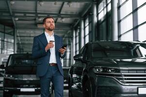 Break, with, coffee and smartphone.,, A businessman is in a car dealership photo