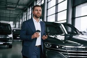 Break, with coffee and smartphone... A ,businessman is in a car dealership photo