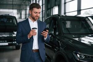 Break, with coffee and smartphone... A businessman is in a car dealership photo