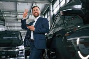 Peace hand gesture. A businessman is in a car dealership photo