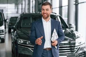 Making a deal, giving ,,a hand, holding notepad. A businessman is in a car dealership photo