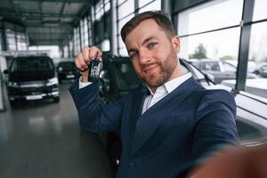 Making, a ,selfie, with keys for new automobile. A businessman is in a car dealership photo
