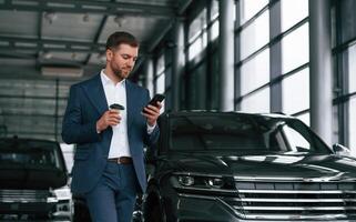 Break, with, coffee and smartphone. A businessman is in a car dealership photo