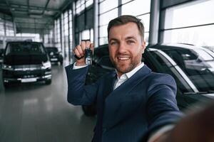 Making a ,selfie, with keys for new automobile. A businessman is in a car dealership photo