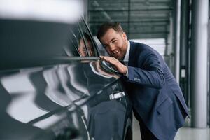 Embracing,, new automobile. A businessman is in a car dealership photo