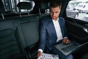 Working,, using laptop. Businessman is in the brand new car photo