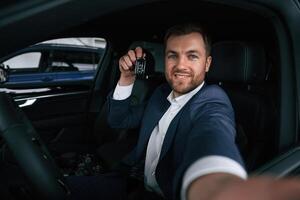 Positive, guy is holding keys. Businessman is in the brand new car photo