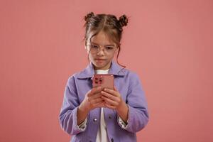 Focused by using smartphone., Cute little girl is against pink background photo