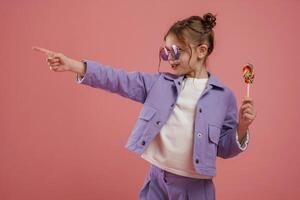 Showing to the side by ,finger.. With candy. Cute little girl is against pink background photo