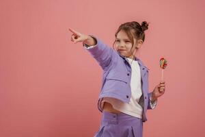 Showing to the side by finger. With candy.,, Cute little girl is against pink background photo