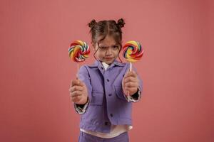 Posing and showing two candies... Cute little girl is against pink background photo