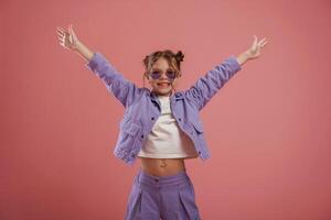 Smiling, with hands up and on the sides. Cute little girl is against pink background photo
