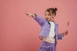 Showing to the side, by finger. With candy. Cute little girl is against pink background photo