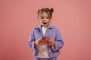 Surprised, using ,smartphone. Cute little girl is against pink background photo