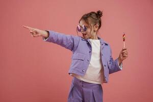 Showing ,to the side by finger. With candy. Cute little girl is against pink background photo