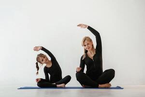 Warm up ,exercises, for hands and spine. Mother and little daughter are in fitness clothes on yoga mat photo