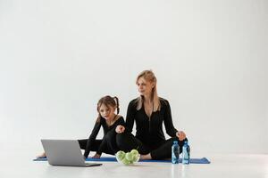 Laptop,,, apples and bottles of water on the floor. Mother and little daughter are in fitness clothes on yoga mat photo