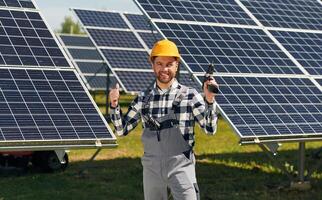 Drill in hand. Engineer with photovoltaic solar panels outdoors at daytime photo
