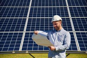 Reading the plan on paper. Engineer with photovoltaic solar panels outdoors at daytime photo