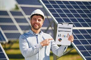 Pointing, to, the ,notepad with diagrams and graphs. Engineer with photovoltaic solar panels outdoors at daytime photo