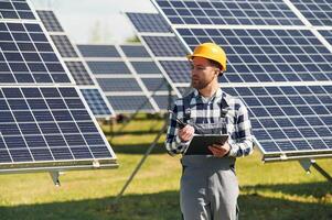 Using walkie talkie and,,, holding notepad. Engineer with photovoltaic solar panels outdoors at daytime photo