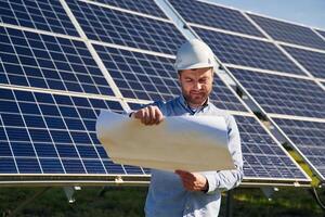 Reading the plan on paper... Engineer with photovoltaic solar panels outdoors at daytime photo