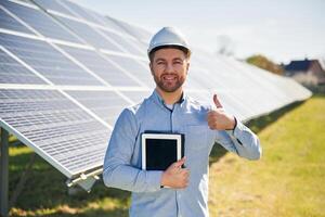 Digital tablet in hand. ..Engineer with photovoltaic solar panels outdoors at daytime photo