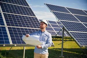 Reading the plan on paper.. Engineer with photovoltaic solar panels outdoors at daytime photo
