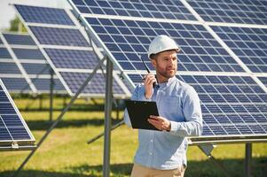 Using walkie talkie and holding notepad.. Engineer with photovoltaic solar panels outdoors at daytime photo