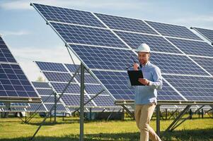 Using walkie talkie and holding notepad... Engineer with photovoltaic solar panels outdoors at daytime photo