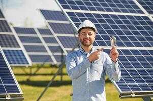 Smiling, and ,holding bulb. Engineer with photovoltaic solar panels outdoors at daytime photo