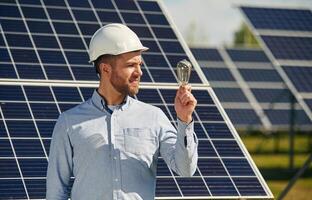 Bulb ,in ,hand. Engineer ,,with photovoltaic solar panels outdoors at daytime photo
