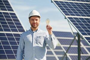 Bulb in hand. Engineer, with photovoltaic solar panels outdoors at daytime photo
