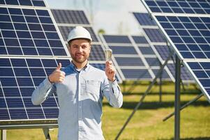 Smiling and holding,, bulb. Engineer with photovoltaic solar panels outdoors at daytime photo