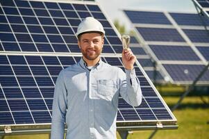 Bulb, in hand. Engineer with photovoltaic solar panels outdoors at daytime photo