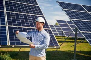 Reading the, plan, o,n paper. Engineer with photovoltaic solar panels outdoors at daytime photo