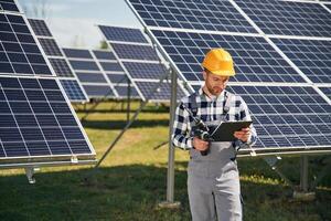 On, the field with, notepad in hands. Engineer with photovoltaic solar panels outdoors at daytime photo