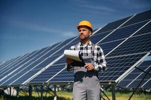 On the field with ,notepad, in hands. Engineer with photovoltaic solar panels outdoors at daytime photo
