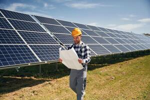 Big paper with plan, reading. Engineer with photovoltaic solar panels outdoors at daytime photo