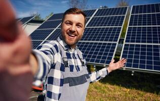 Making a selfie, smiling. Engineer with photovoltaic solar panels outdoors at daytime photo