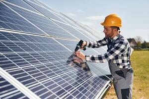 Installation process, ,with drill. Engineer with photovoltaic solar panels outdoors at daytime photo