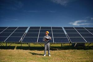 Black notepad in hands.. Engineer with photovoltaic solar panels outdoors at daytime photo