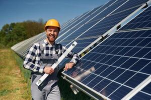 Portrait, holding leveler, tool. Engineer with photovoltaic solar panels outdoors at daytime photo