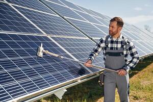 Mop in hands. Cleans, the surface. Engineer with photovoltaic solar panels outdoors at daytime photo