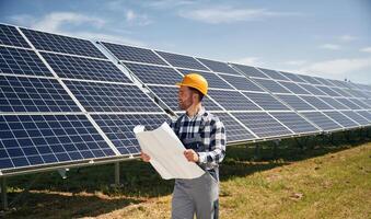 grande papel, con plan, lectura. ingeniero con fotovoltaica solar paneles al aire libre a tiempo de día foto
