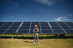 Black ,notepad in hands. Engineer with photovoltaic solar panels outdoors at daytime photo