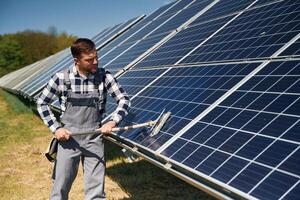 Mop, in hands. Cleans the surface. Engineer with photovoltaic solar panels outdoors at daytime photo