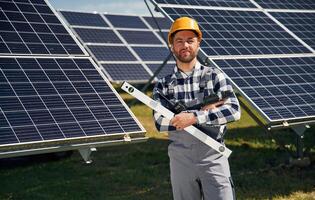 Portrait,, holding leveler tool. Engineer with photovoltaic solar panels outdoors at daytime photo